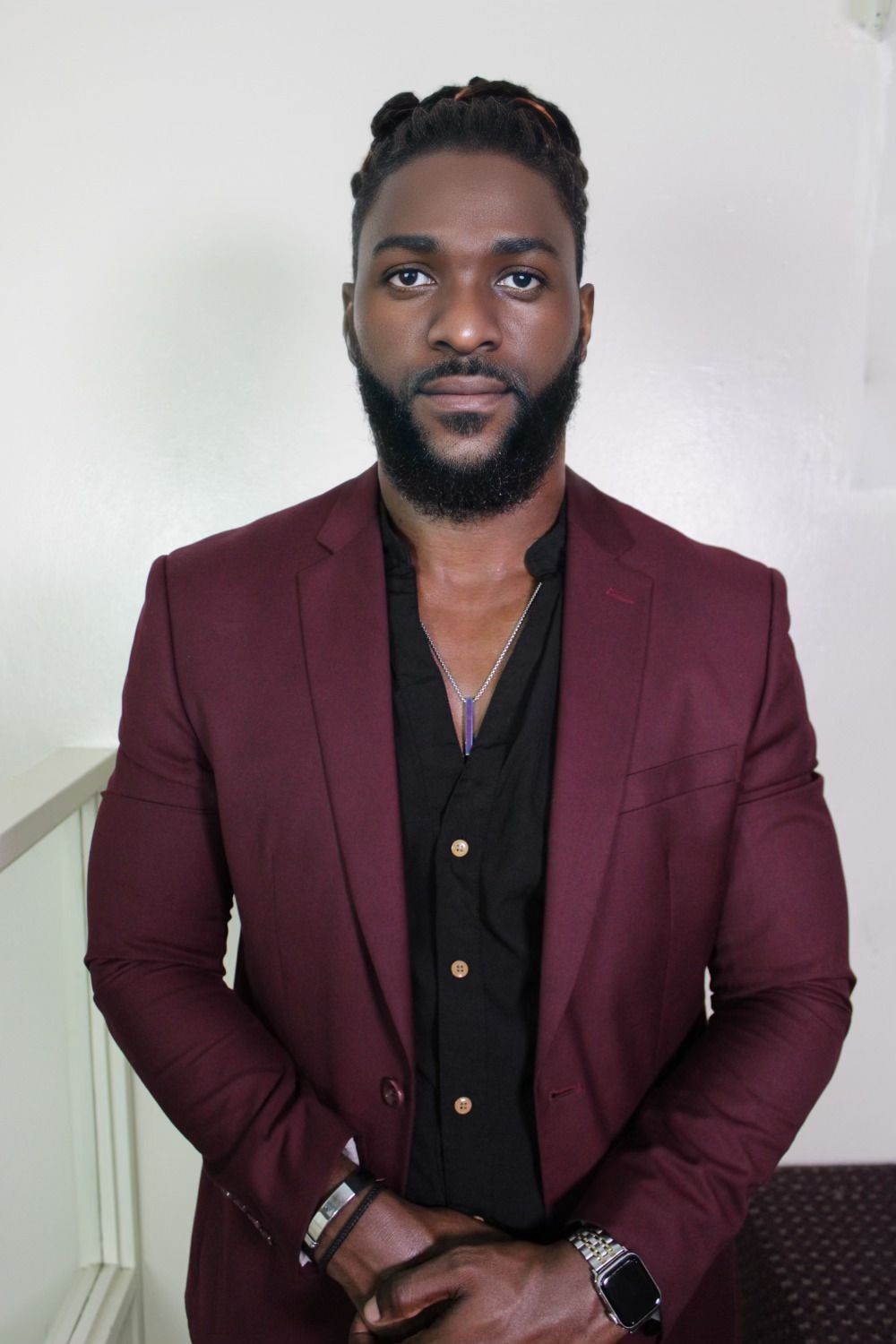 Man in burgundy blazer posing against a plain background, wearing a necklace and smartwatch.